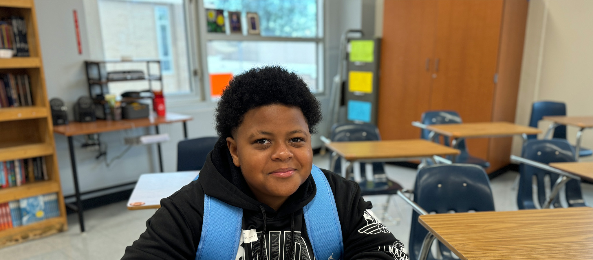 Student smiling in classroom with a backpack